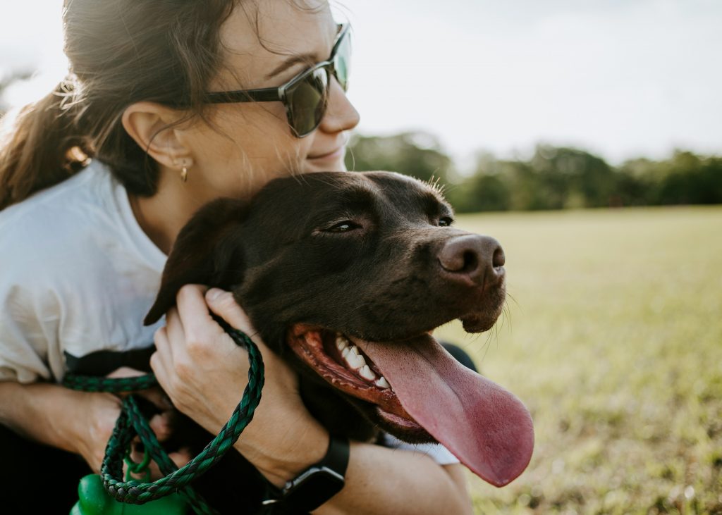 A woman hugging a black dog in a green field. 