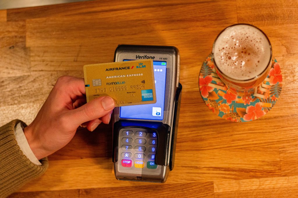 A person makes a card payment using 'tap' on an Eftpos machine. There is a coffe in a glass on a floral plate. 